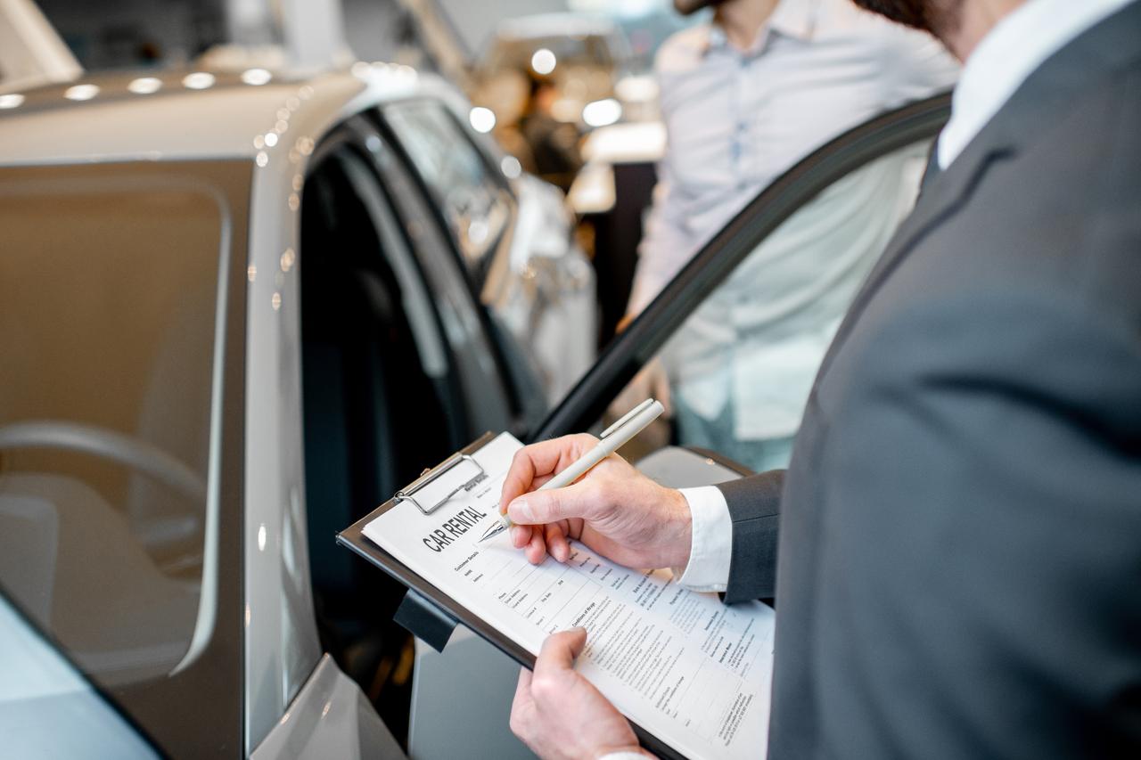 A manager filling car rental documents standing in the showroom with car on the background. (Adobe Stock Photo)