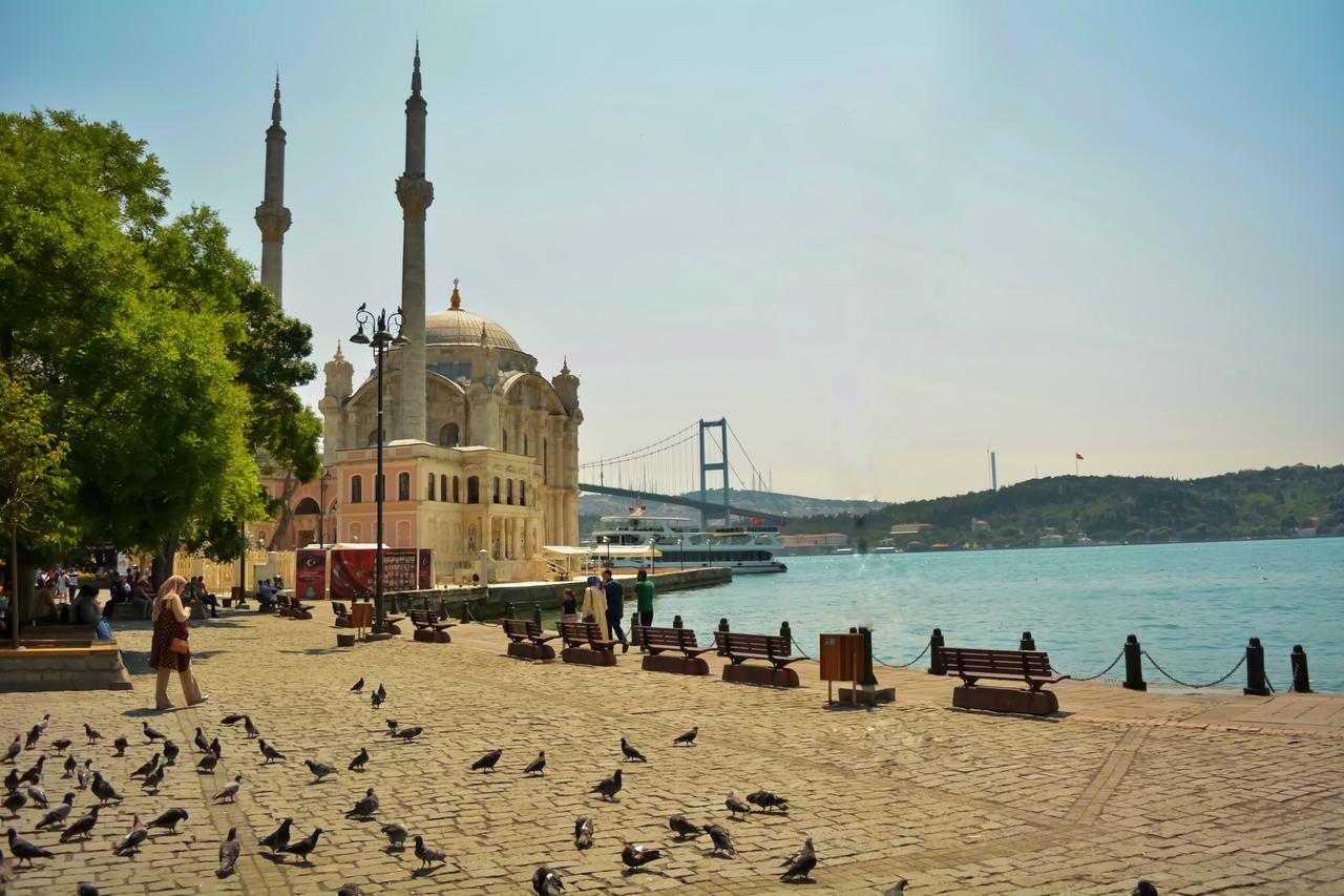 People walk along the Bosphorus waterfront by Ortakoy Mosque in Istanbul, Türkiye. (Adobe Stock Photo)