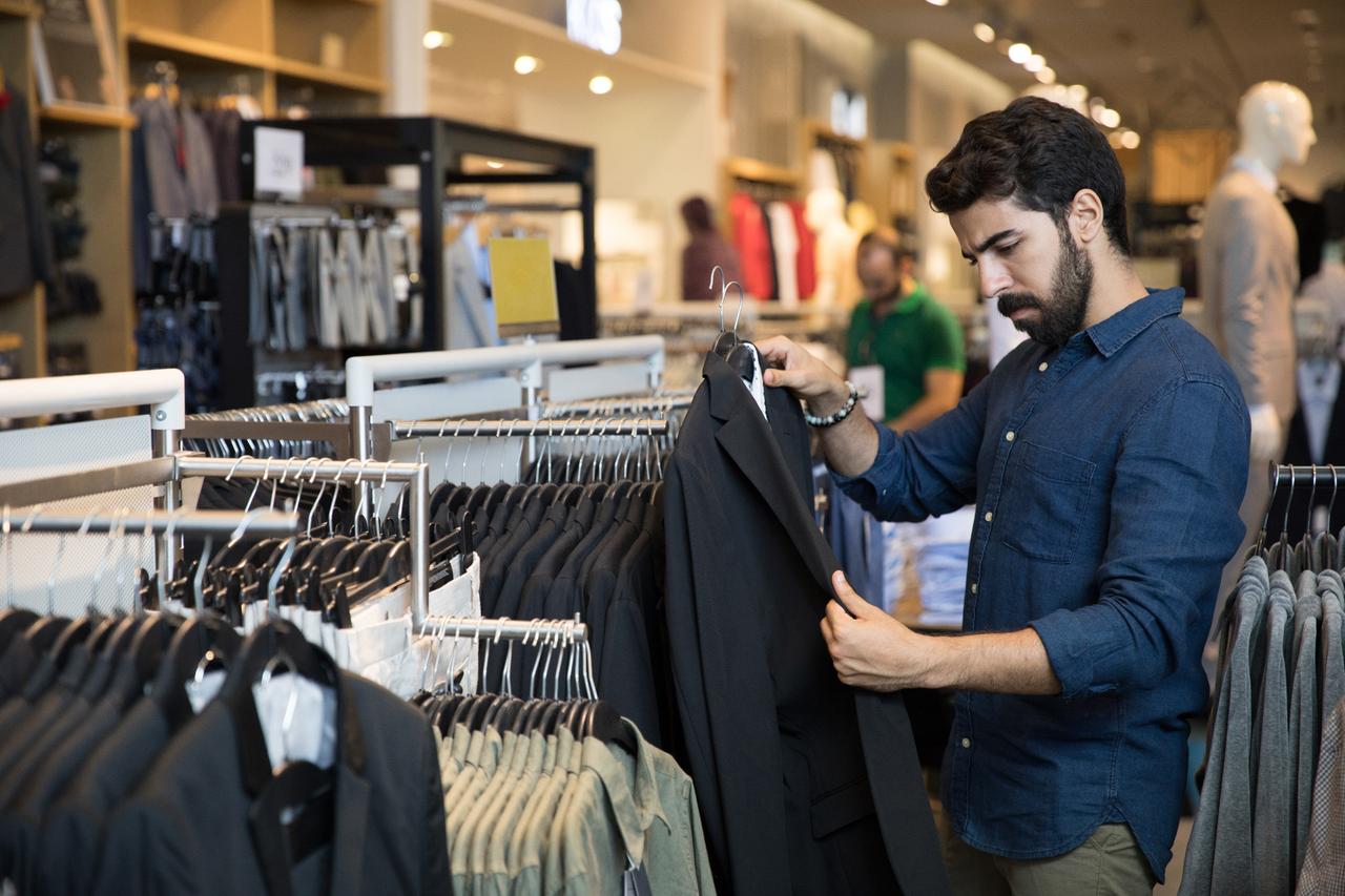A customer examines a suit jacket at a clothing store. (Adobe Stock Photo)