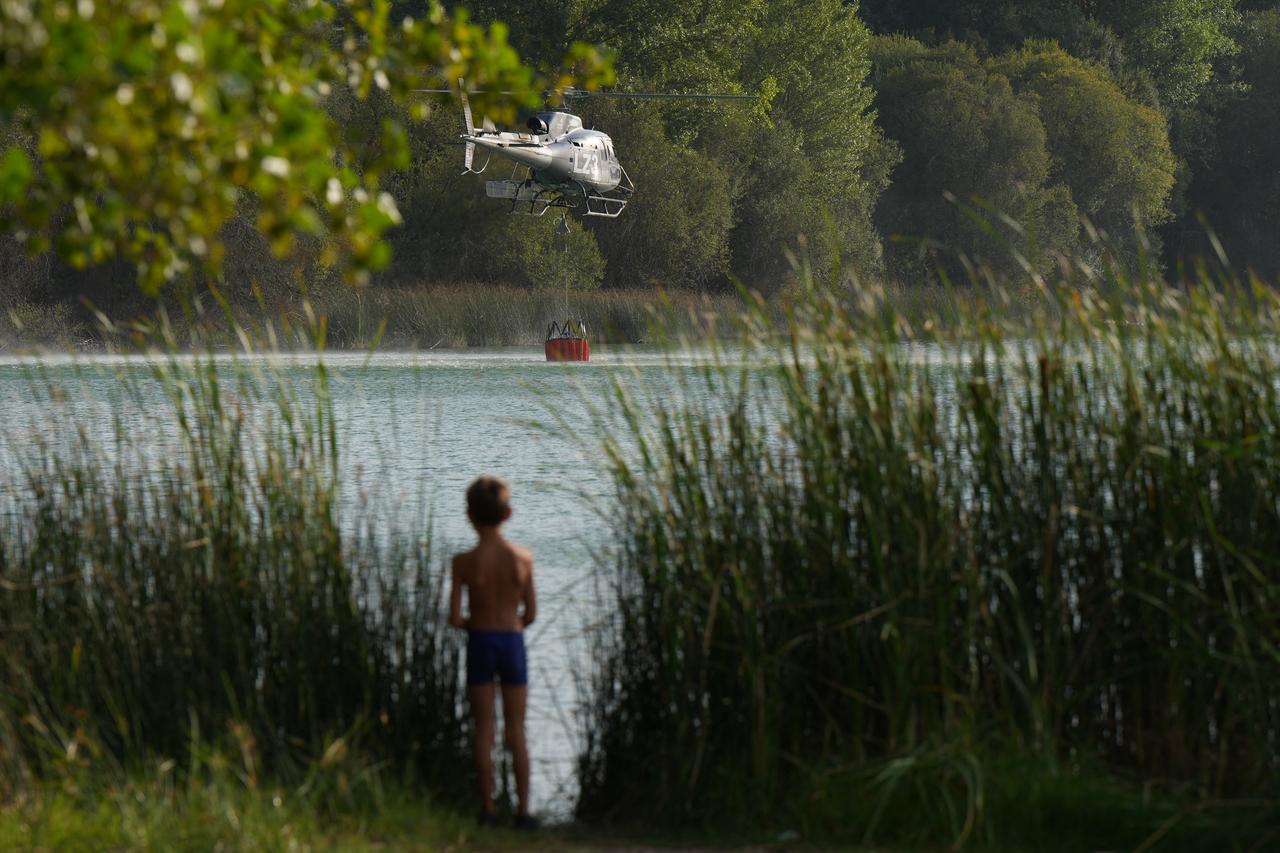 A boy watches a helicopter loading water to battle a wildfire in the municipality of Carucedo, Spain, August 11, 2025. (AFP Photo)