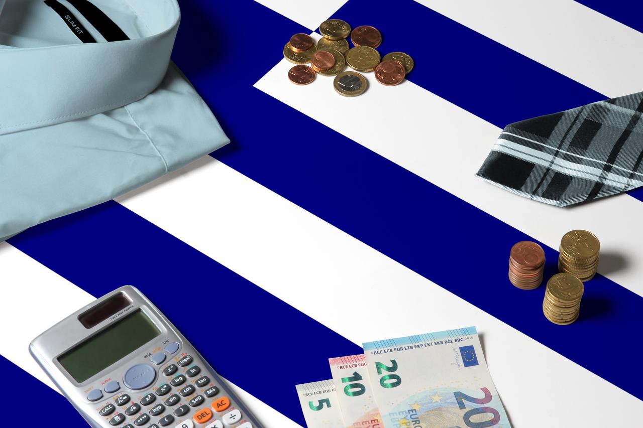 Greece flag on minimal money concept table. Coins and financial objects on flag surface. (Adobe Stock Photo)