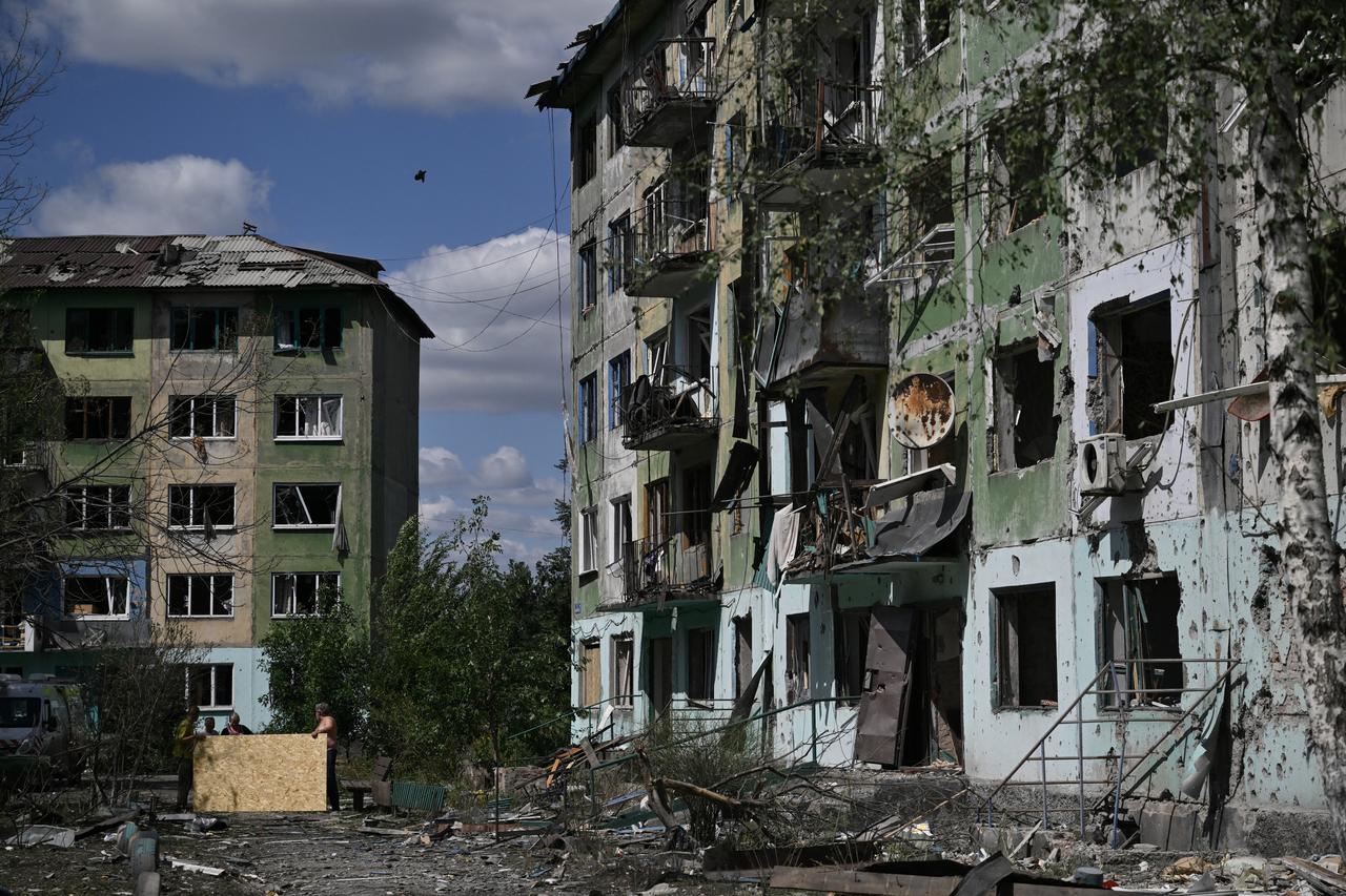 Residents carry sheets of plywood to cover broken windows in a heavily damaged residential building following a Russian strike in the town of Bilozerske, Donetsk region on August 12, 2025. (AFP Photo)
