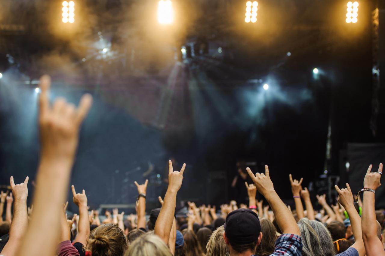 A group of people at a concert raise their hands, making the heavy metal rock sign with their fingers. (Adobe Stock Photo)