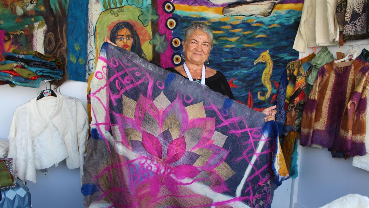 Ayfer Gulec displays one of her handmade felt textiles at her workshop, surrounded by vibrant garments and wall hangings, Izmir, Türkiye, September 27, 2024. (Photo by Ankara Ulus)