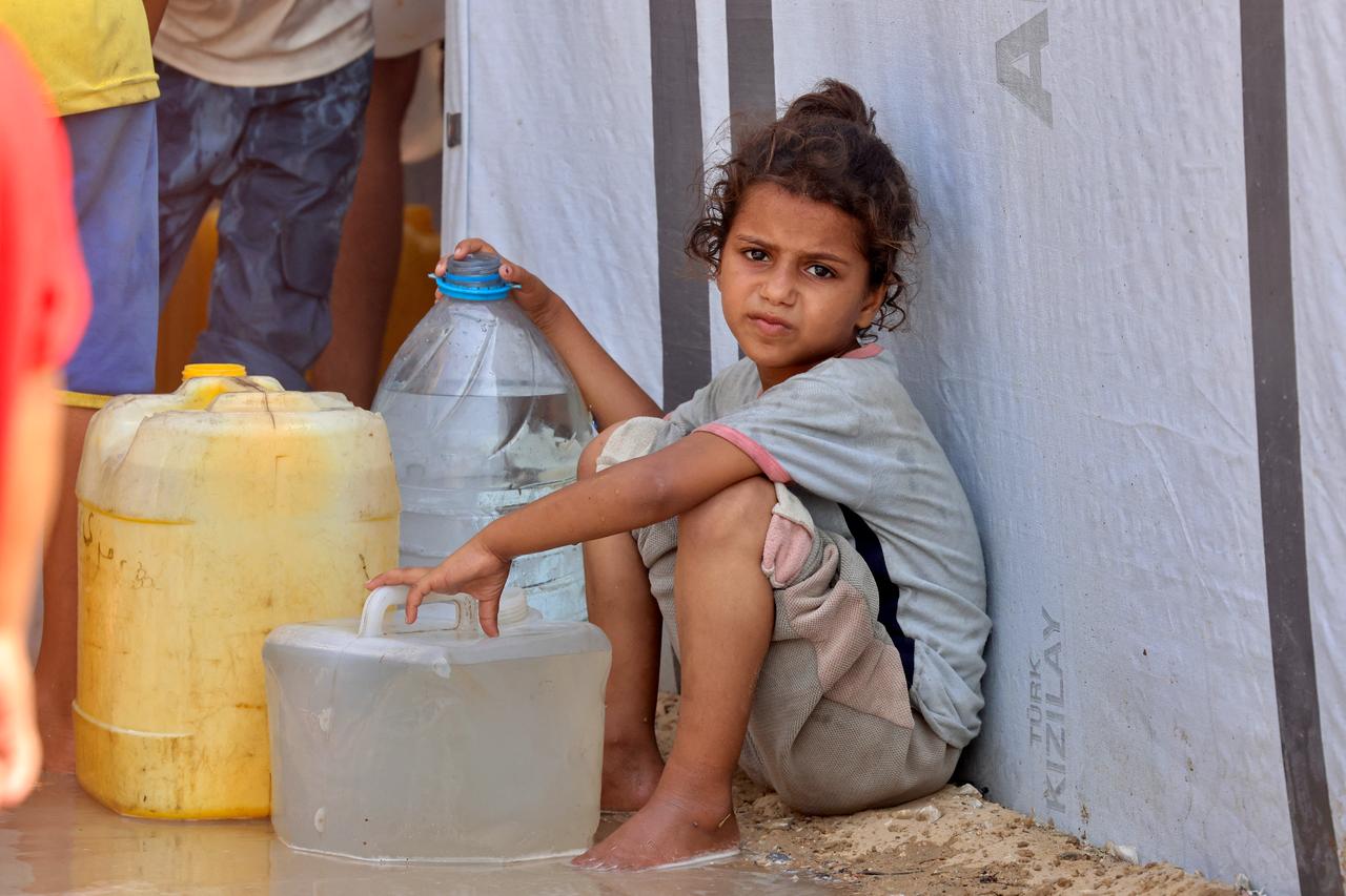 A girl sits by water containers while displaced Palestinians wait to collect water in the Mawasi area of Khan Yunis, Palestine, August 14, 2025. (AFP Photo)