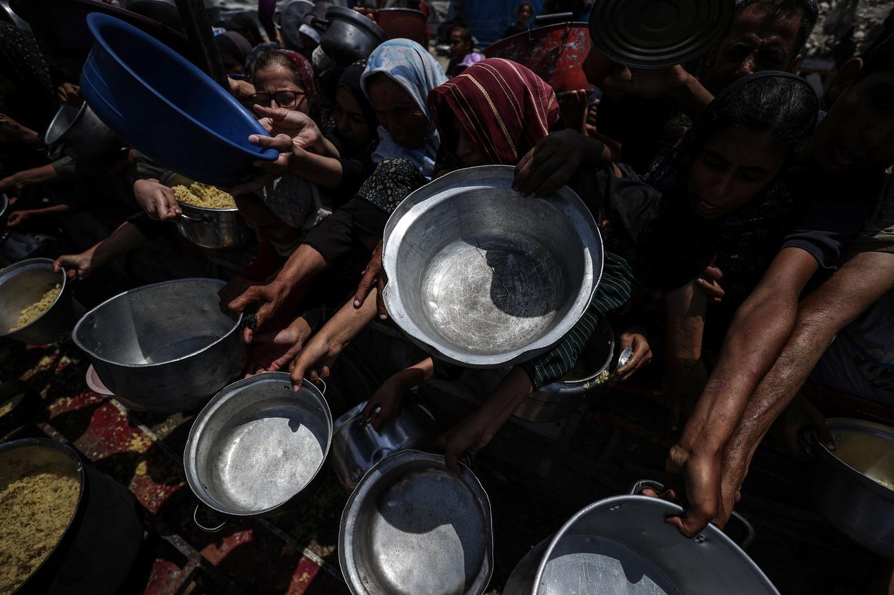 Palestinians wait with pots in their hands as a charitable organization distributes food to Palestinians suffering food crisis under Israeli blockade in Gaza City, Gaza on August 15, 2025. (AA Photo)