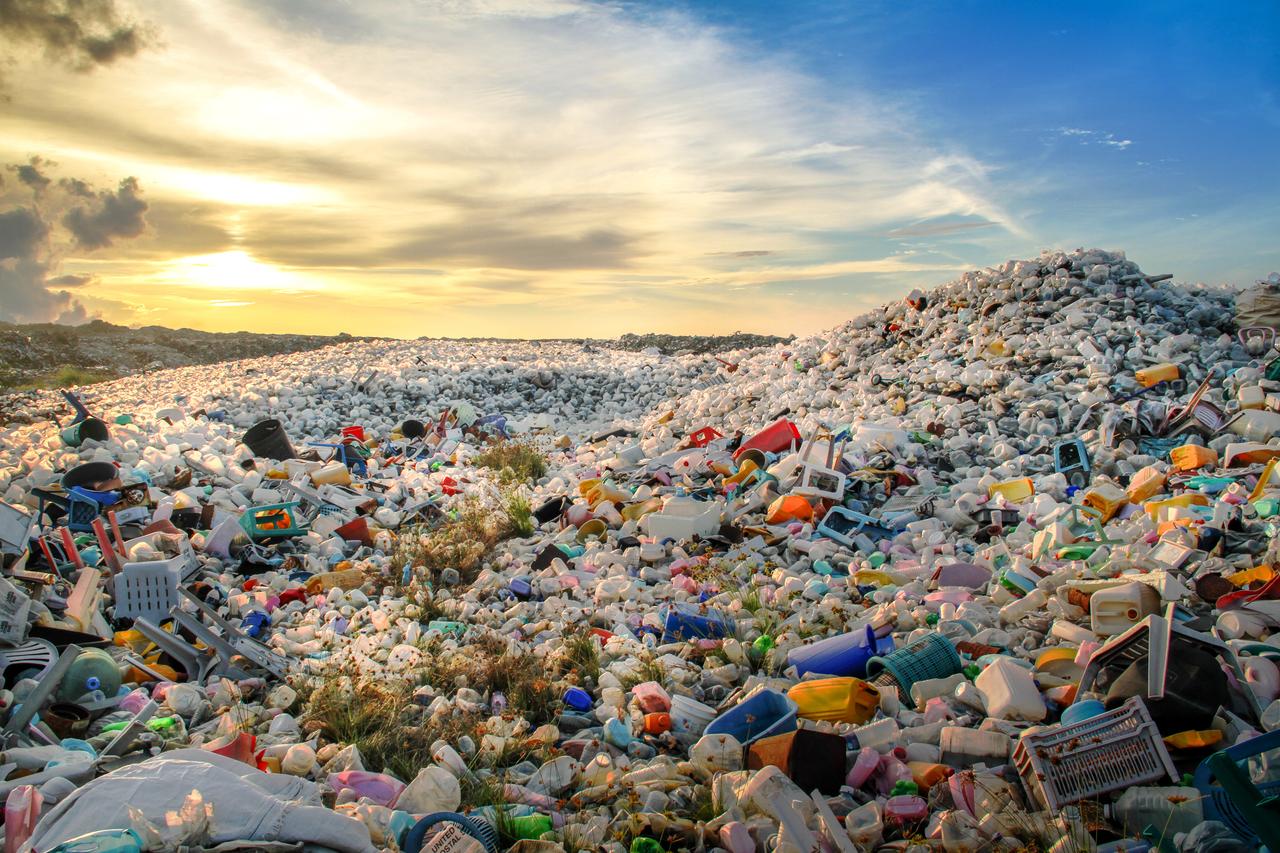 A landfill site filled with discarded single-use plastic containers and household items under a sunset sky, accessed August 15, 2025. (Adobe Stock Photo)