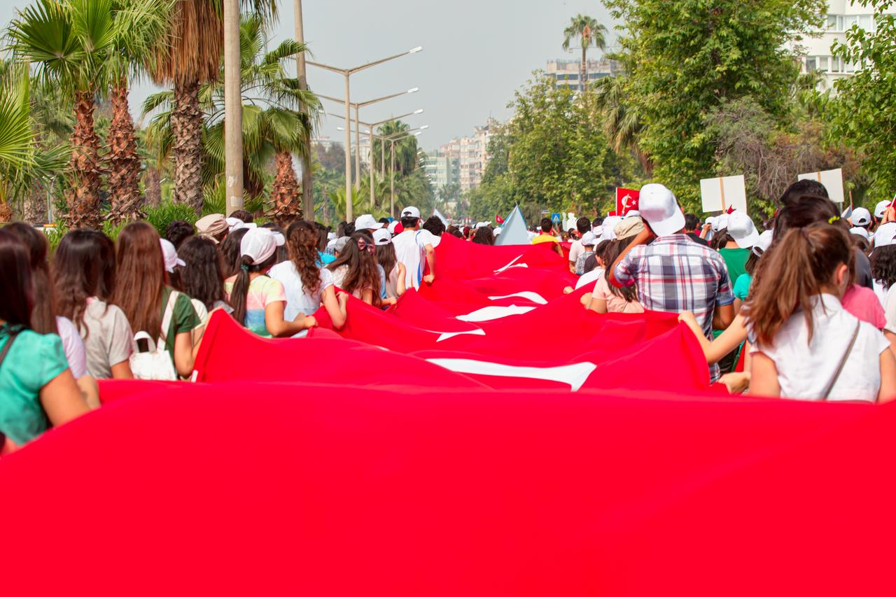 People march while carrying a large Turkish flag during the 19 May Youth and Sports Day celebrations in Türkiye. (Adobe Stock Photo)