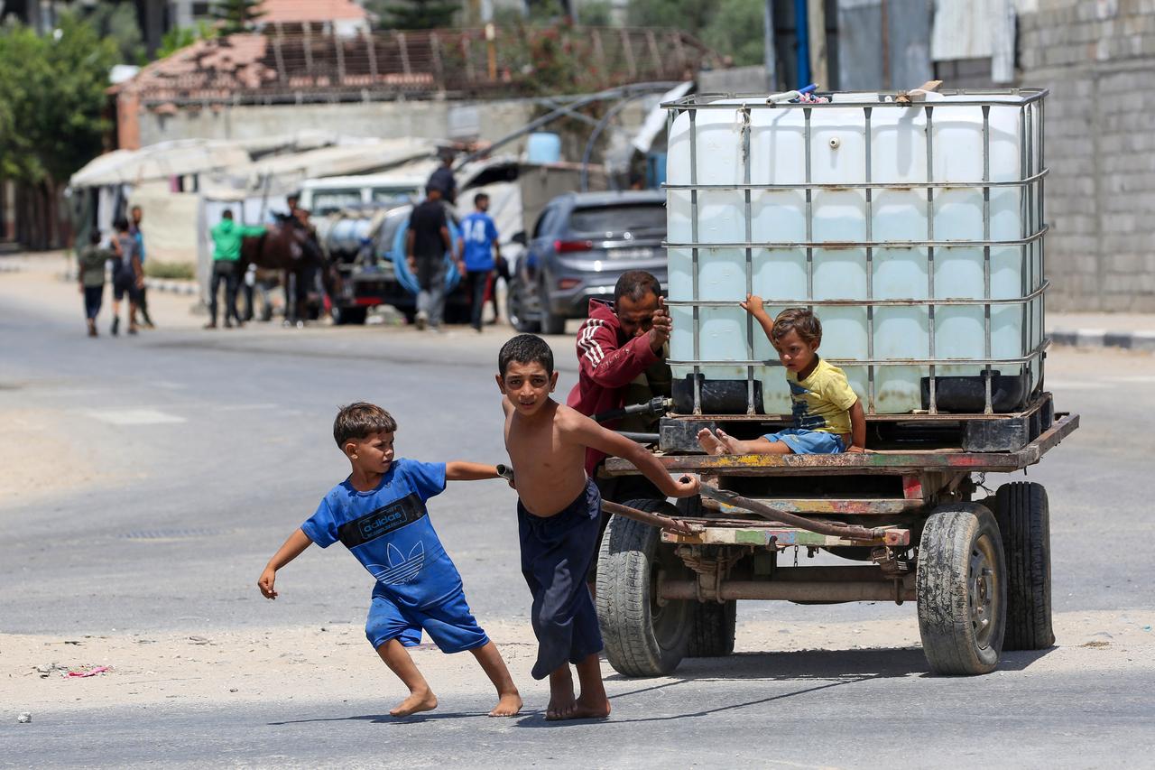 A man and young children push on a cart carrying a water tank at the Bureij camp for displaced Palestinians in the central Gaza Strip, on August 17, 2025. (AFP Photo)