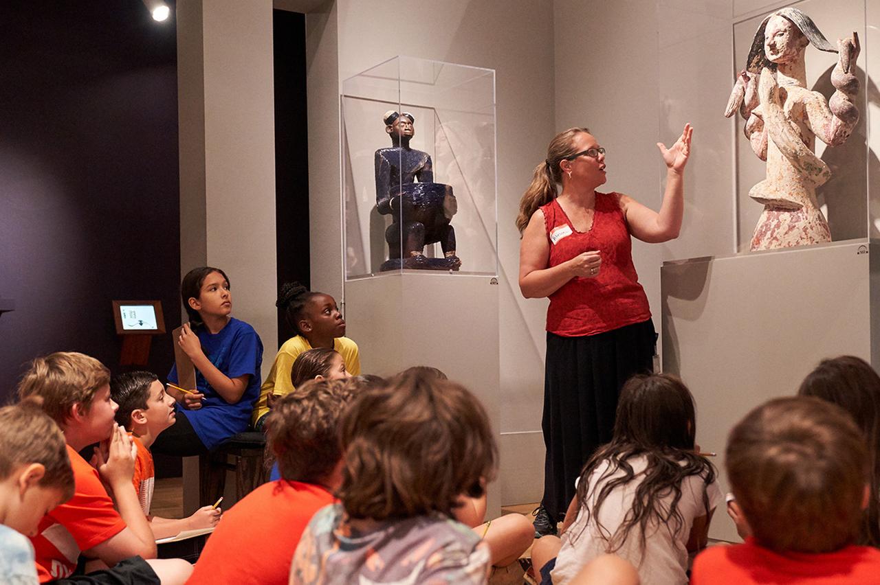 Children listen attentively as a museum educator explains African art pieces at Emory University’s Carlos Museum African Gallery─the gallery houses around 1,600 objects showcasing the vast diversity and cultural heritage of the African continent. (Photo via Emory University Carlos Museum)