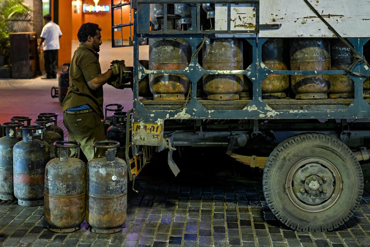 A worker unloads liquified petroleum gas (LPG) cylinders from a truck, parked outside a hotel at the Church Street in Bengaluru on August 2, 2025. (AFP Photo)