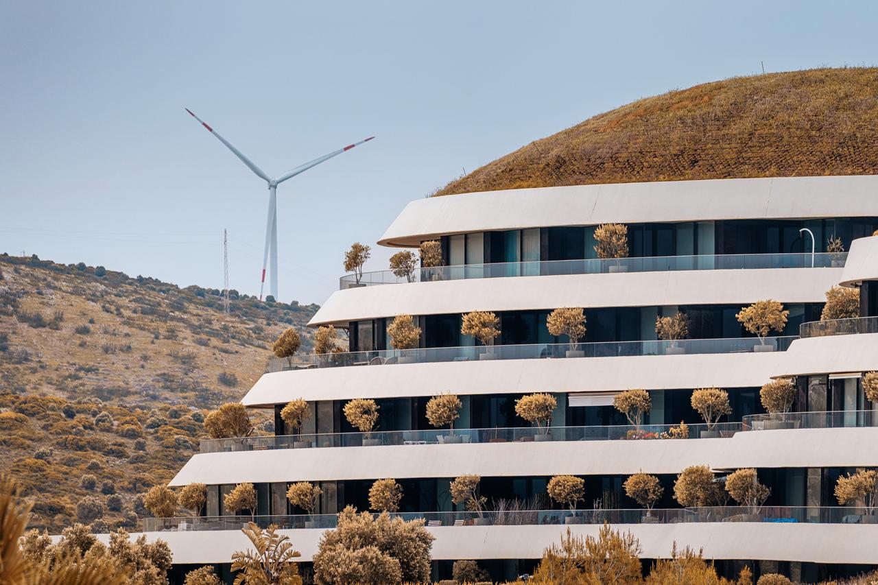 White modern building with green roof with wind turbine can be seen in Cesme, Türkiye on 28 April 2025. (Adobe Stock Photo)