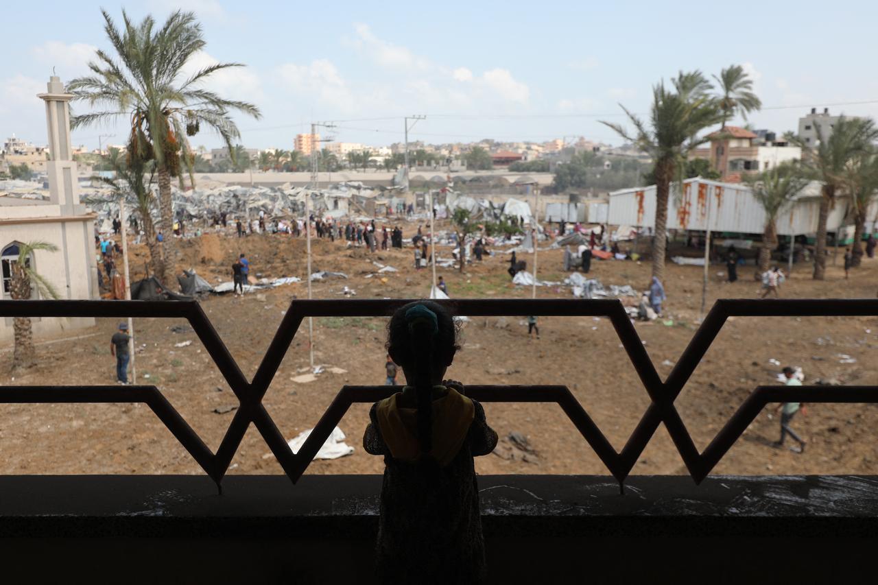 A displaced girl watches from the balcony of a house as Palestinians inspect the damage around an impact crater, left behind after an Israeli strike, at a camp for internally displaced people in the central Gaza Strip, August 21, 2025. (AFP Photo)