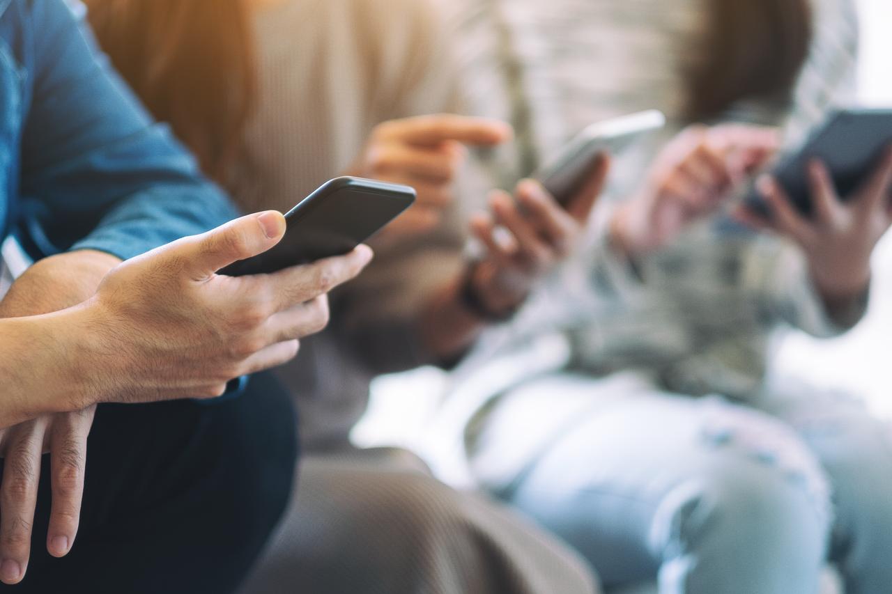 People are interacting and looking at their smartphones together. (Adobe Stock Photo)