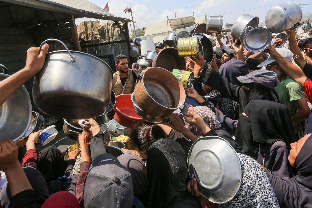 Palestinians, including children wait in line to receive hot meals distributed by the charity organization at Al-Mawasi area in Khan Yunis, Gaza on August 21, 2025. (AA Photo)