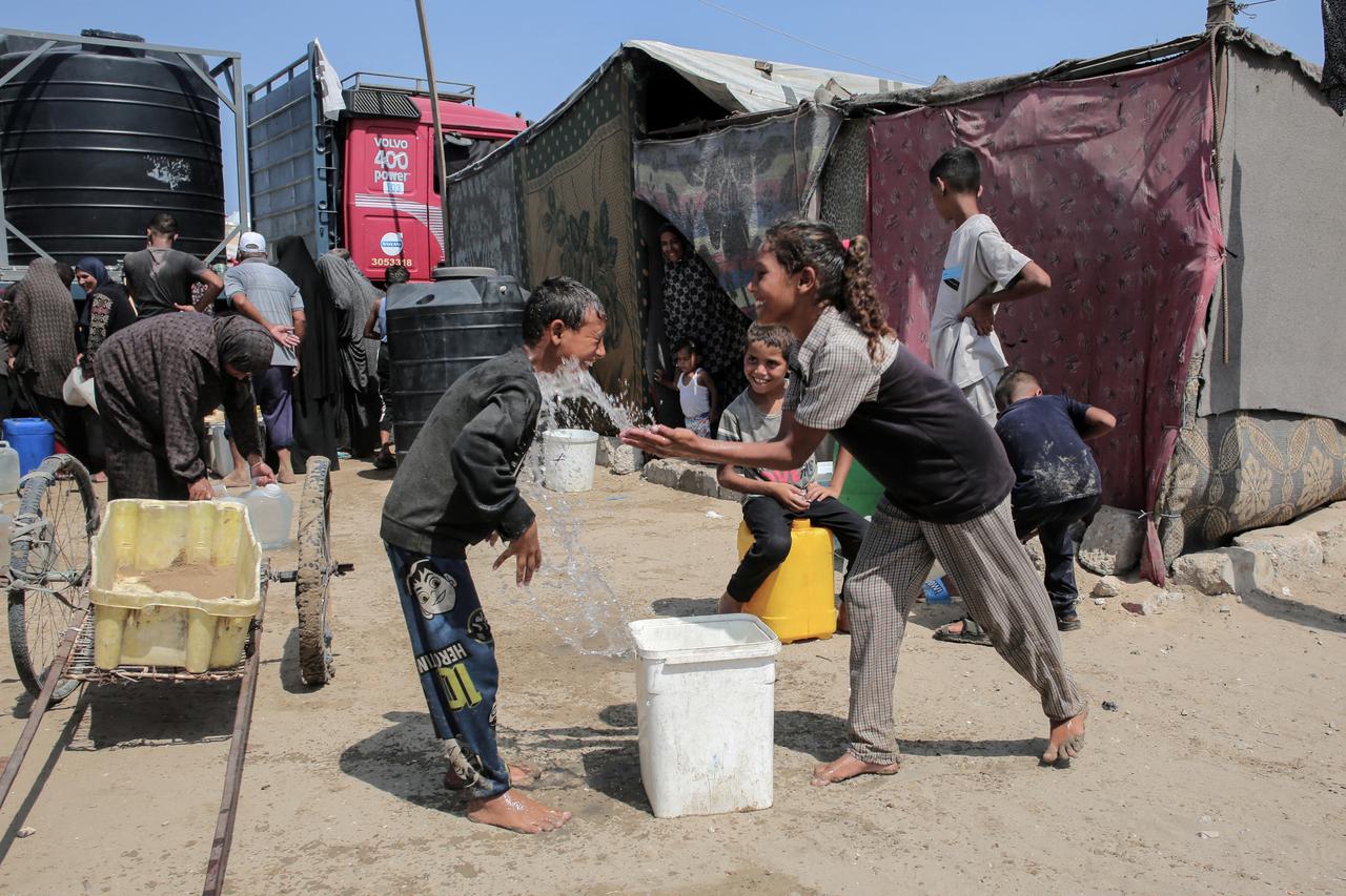 A girl splashes water on a boy as displaced Palestinians gather to fill water containers in the Mawasi area of Khan Yunis, on August 14, 2025. (AFP Photo)