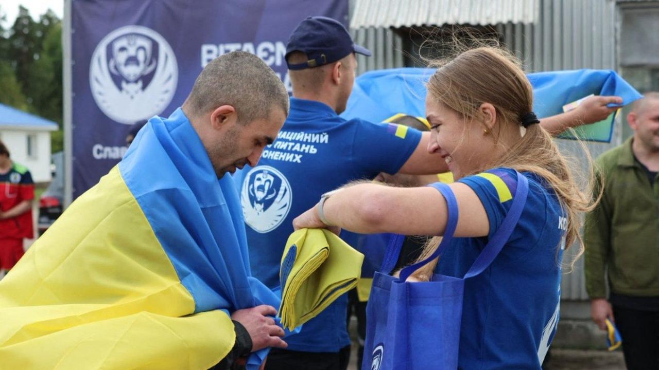 In this handout photograph taken and released by the Coordination Headquarters for the Treatment of Prisoners of War on August 24, 2025, staff member of the Coordination Headquarters for the Treatment of Prisoners gives a Ukrainian national flag to a Ukrainian prisoner of war (POW) following an exchange of prisoners at an undisclosed location in Ukraine, amid the Russian invasion in Ukraine. (Coordination Headquart / AFP Photo)