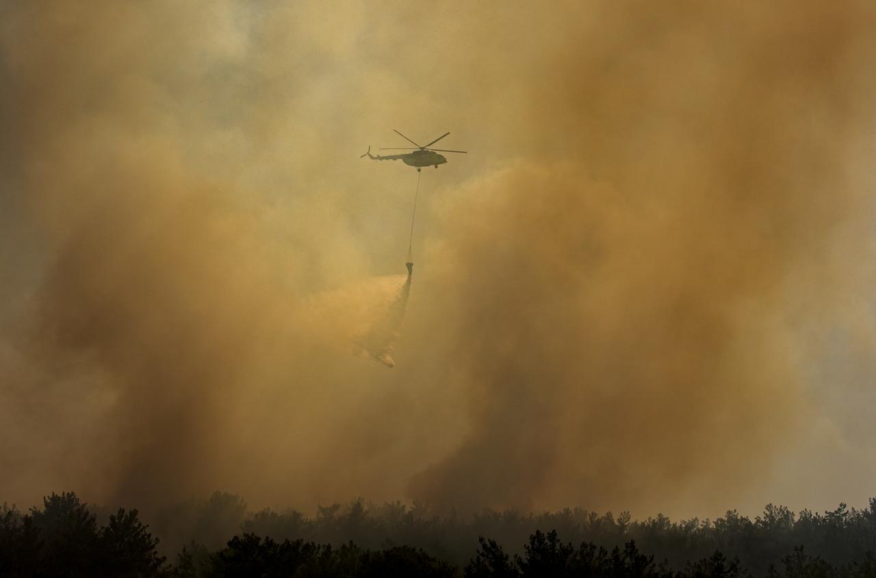 A firefighting helicopter drops water over a wildfire that started in farmland and spread to a forest area as it is being tackled with both aerial and ground firefighting efforts in Menderes district of Izmir, Türkiye, August 22, 2025.