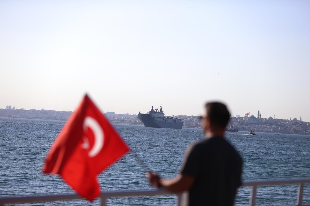 A man holds the Turkish flag as TCG Anadolu, TCG Orucreis, TCG Istanbul, TCG Heybeliada and other vessels sail during a parade in Istanbul, Türkiye, August 24, 2025. (AA Photo)