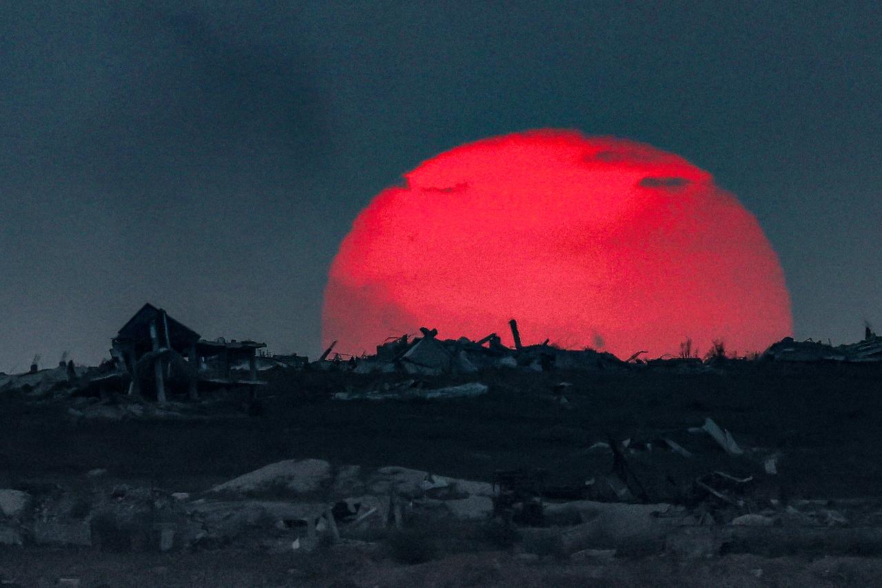 This picture taken from a position on the Israeli border with the Gaza Strip, shows the sun setting behind destroyed buildings in the embattled territory, on August 27, 2025. (AFP Photo)
