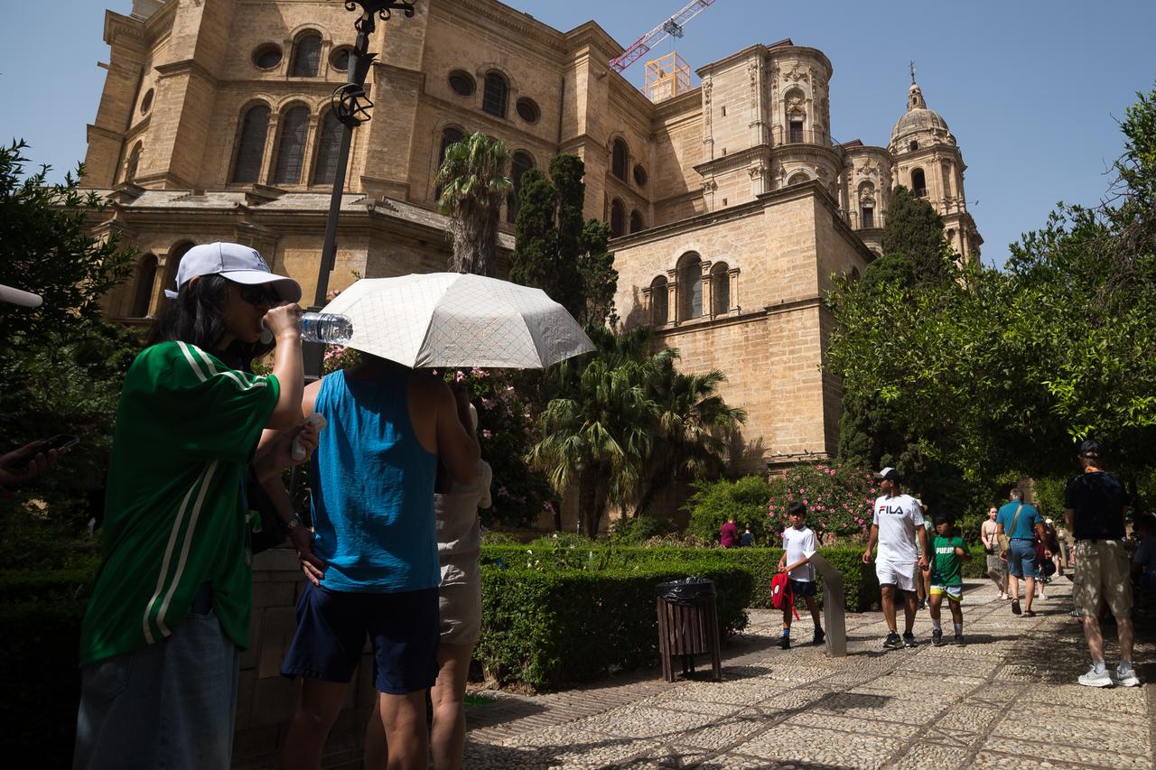 A tourist holds an umbrella to protect himself from the sun, and other drinks water to cool off, during a hot summer day in Malaga, Spain, August 5, 2025. (AA Photo)
