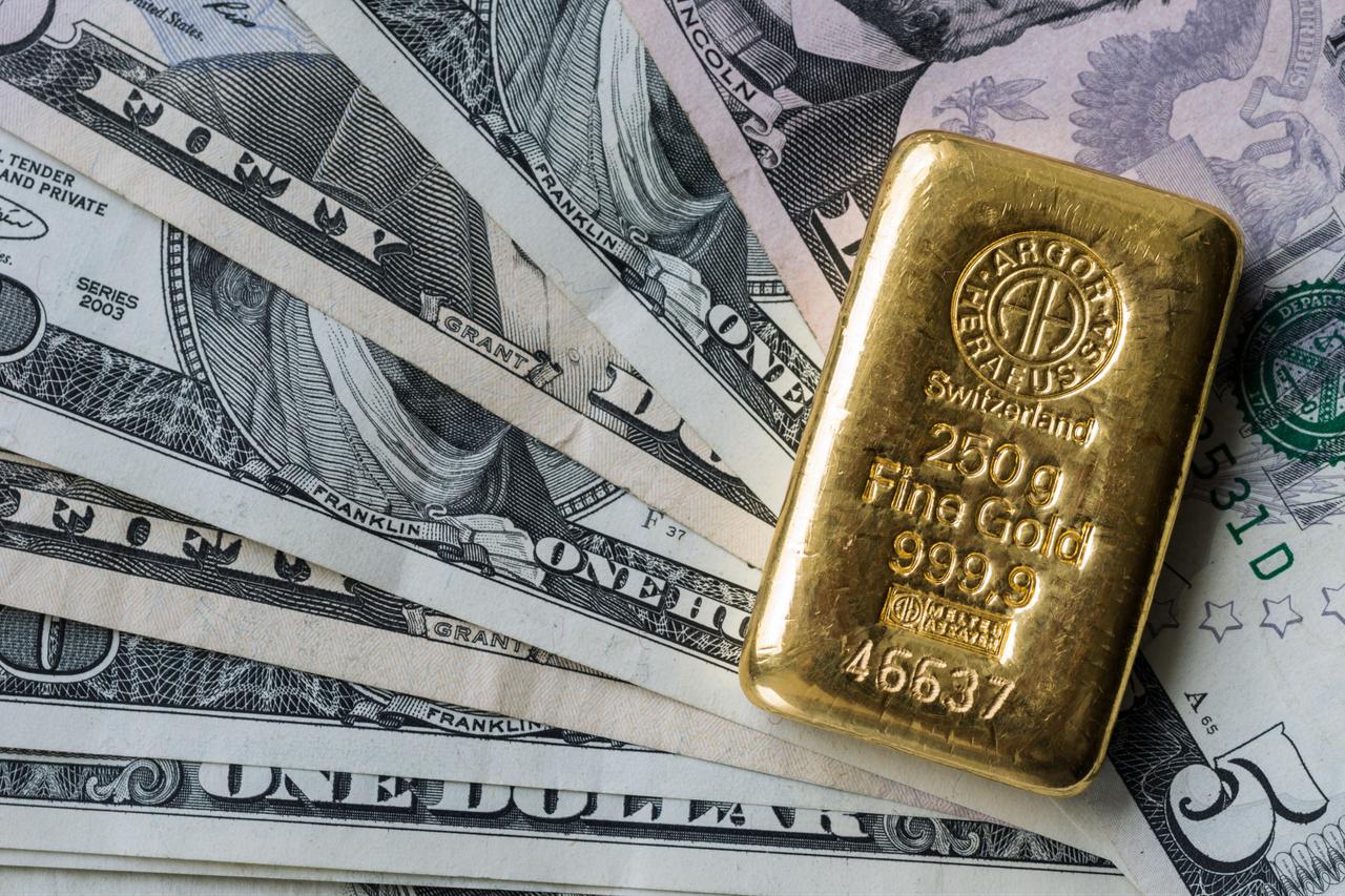 A 250-gram Swiss gold bar rests on U.S. dollar banknotes. (Adobe Stock Photo)
