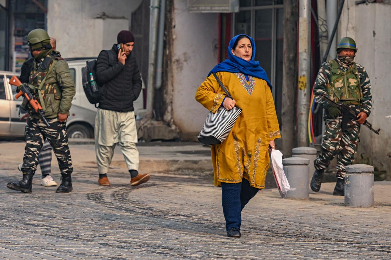 People walk along a street as Indian paramilitary personnel patrol in Srinagar on December 11, 2023. (AFP Photo)