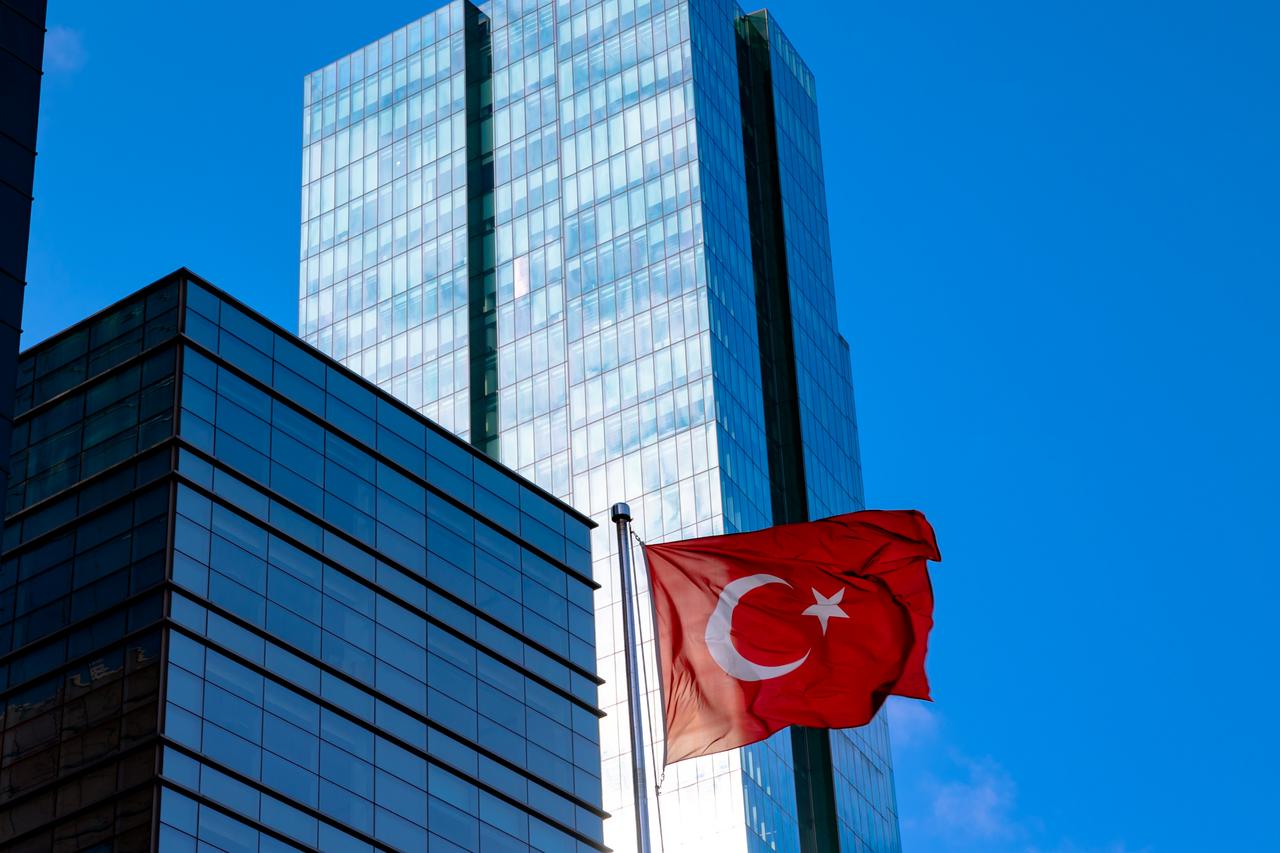 A Turkish flag waves in front of modern office buildings in Istanbul, Türkiye. (Adobe Stock Photo)