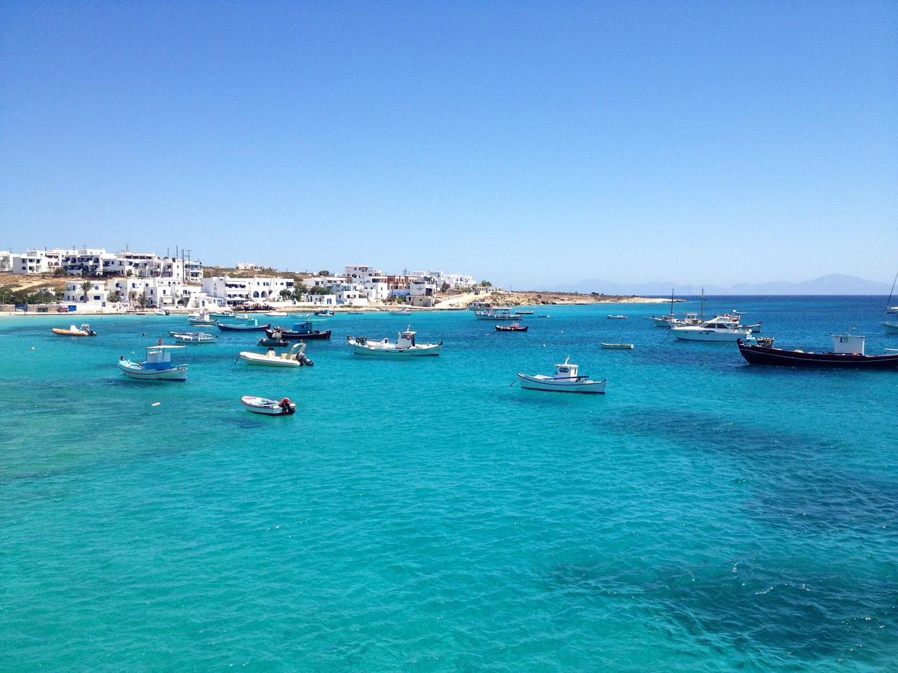 Fishing boats anchored in the vivid blue waters off Koufonisia, with the island’s village visible on the shoreline, Cyclades, Greece, accessed September 11, 2025. (Adobe Stock Photo)