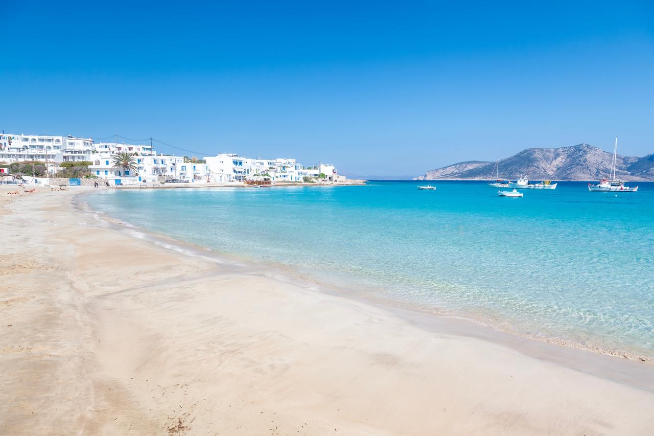 Sandy beach and calm blue sea on Koufonisia, with traditional white buildings lining the coast, Cyclades, Greece, accessed September 11, 2025. (Adobe Stock Photo)