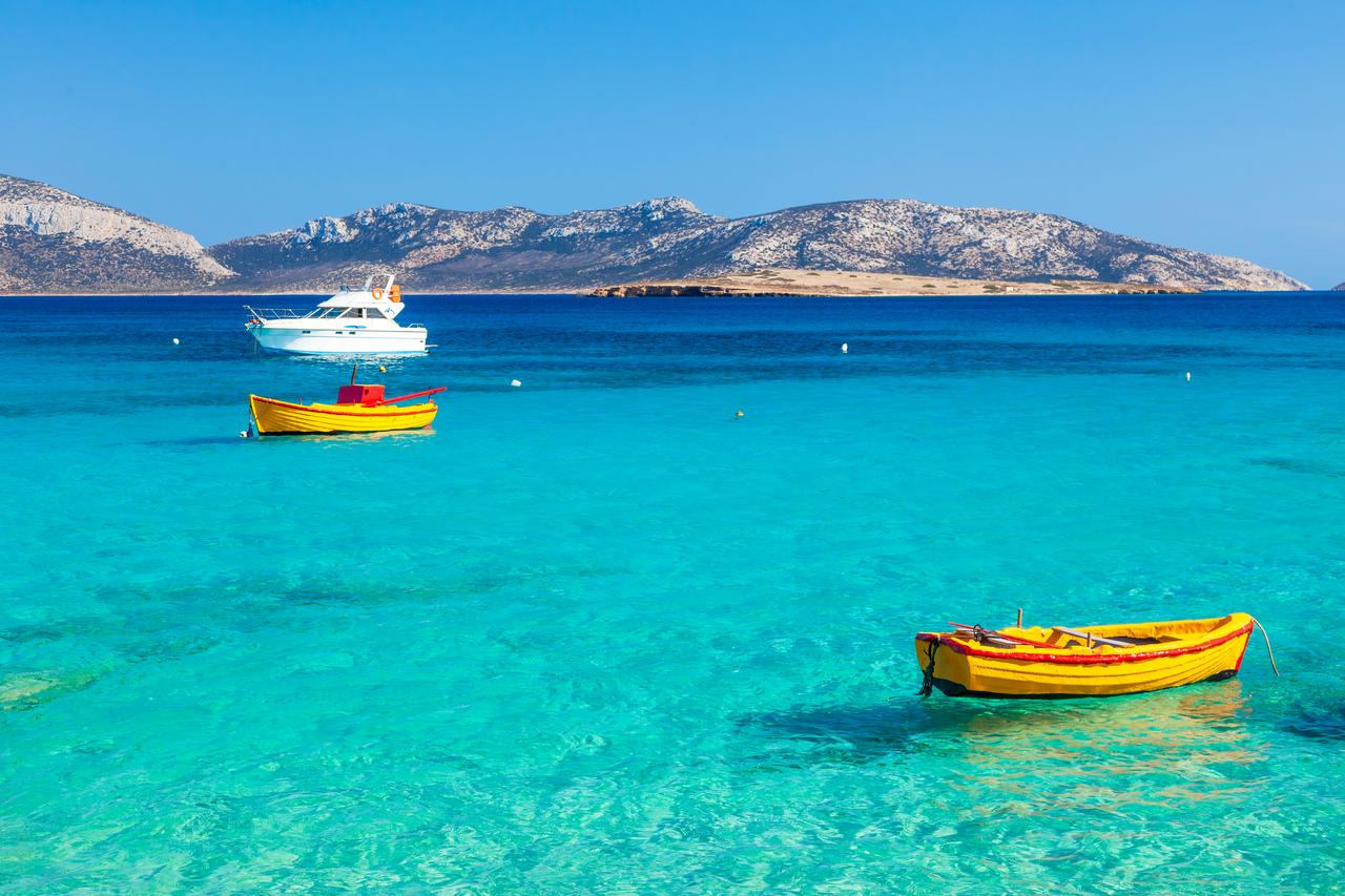 Two yellow fishing boats anchored in the crystal-clear waters of Koufonisia, with the rocky Cycladic landscape in the distance, Greece, accessed September 11, 2025. (Adobe Stock Photo)