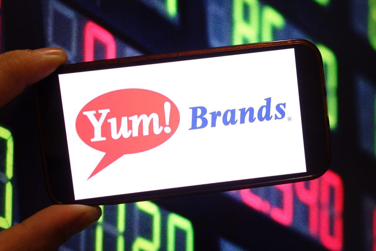 Photo shows a person holding a smartphone displaying the logo of Yum! Brands. (Adobe Stock Photo)
