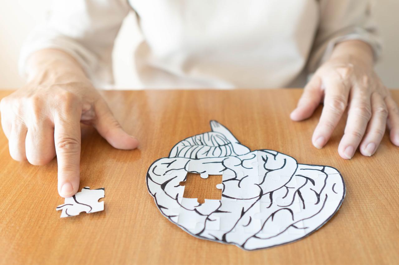An elderly person placing the last missing piece into a jigsaw puzzle shaped like a human brain. (Adobe Stock Photo)