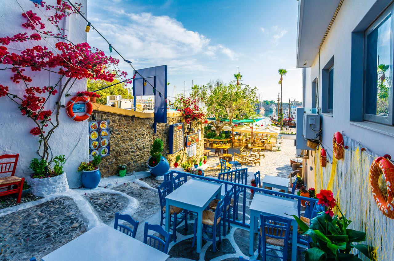 A colorful street with traditional tavernas and outdoor seating near the harbor, Kos, Greece, accessed September 18, 2025. (Adobe Stock Photo)