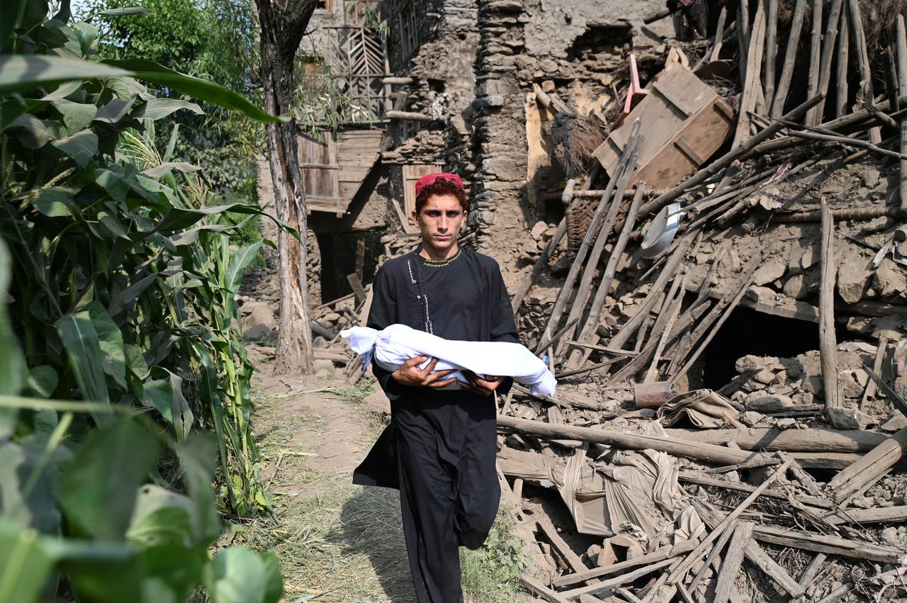 An Afghan boy carries the body of a relative in a shroud as he walks past by a damaged house following earthquakes in the Mazar Dara village of Nurgal, a district of the Kunar Province, in Eastern Afghanistan, Sept. 1, 2025. (AFP Photo)