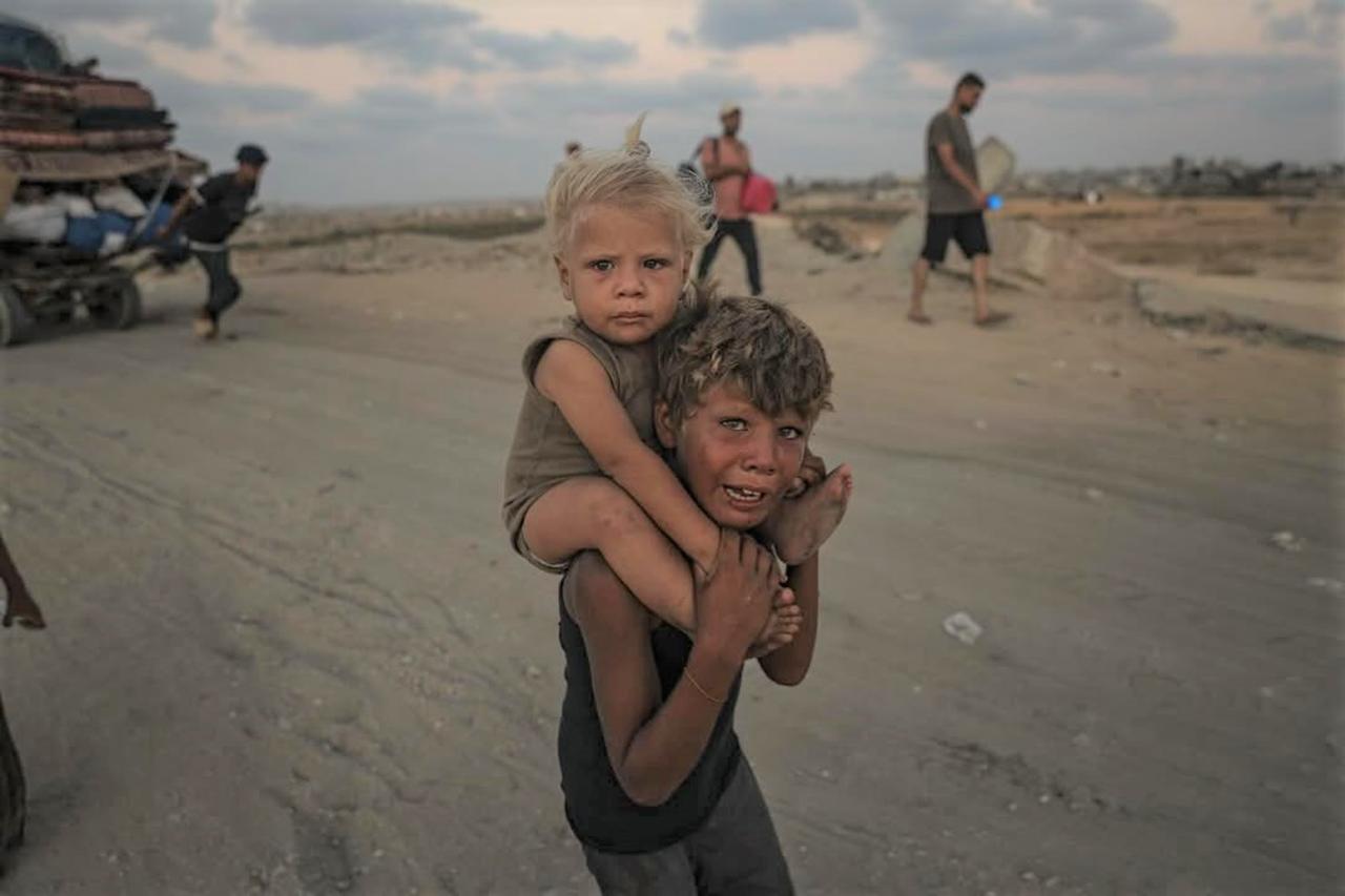 A child carries his younger sister on the long road of displacement from northern Gaza to the south, a scene reflecting the dire humanitarian toll of the war on civilians , September 18, 2025. (Photo courtesy of Ahmed Younis)