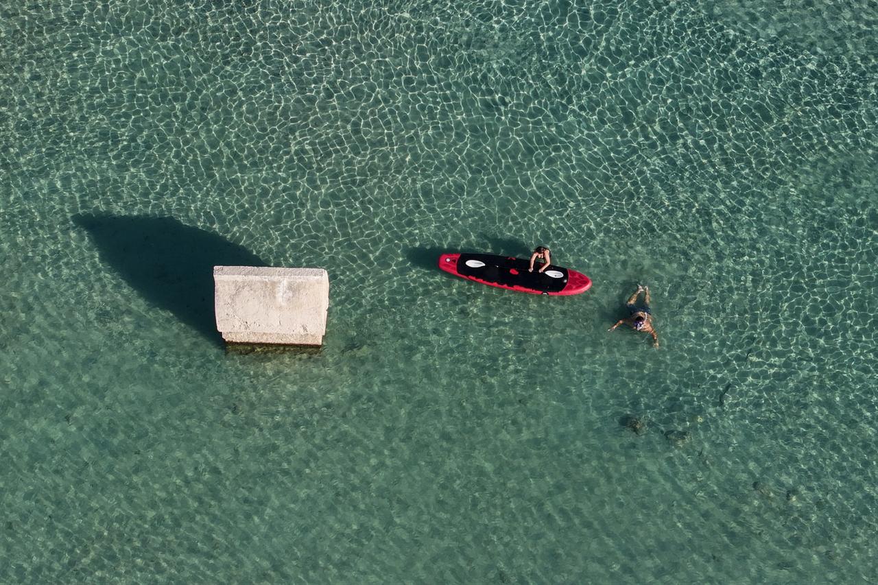 Tourists swim and paddleboard near an ancient Lycian sarcophagus lying partly submerged in Kalekoy, Antalya, Türkiye, Sept. 21, 2025. (AA Photo)