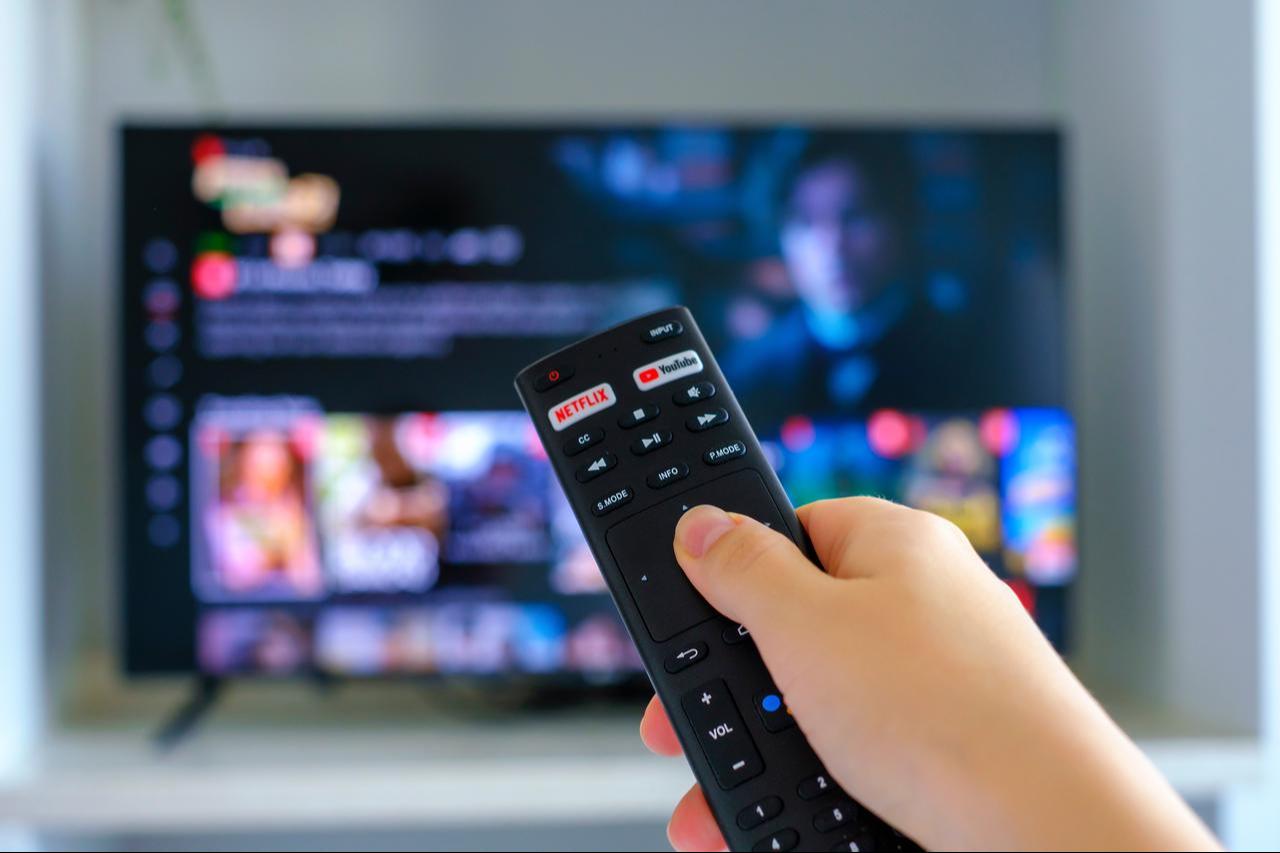 A viewer uses a smart TV remote with direct access buttons for Netflix and YouTube. (Adobe Stock Photo)