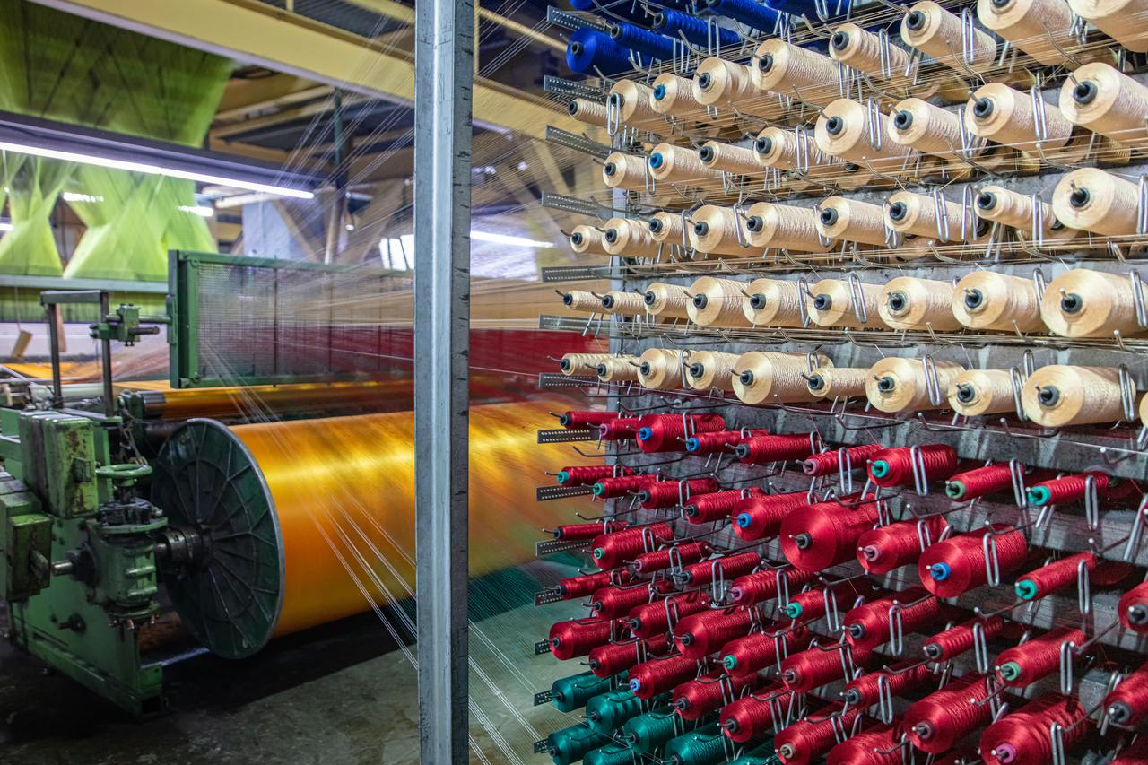 Colorful yarn spools feeding into automated looms at a carpet factory in Türkiye. (Adobe Stock Photo)