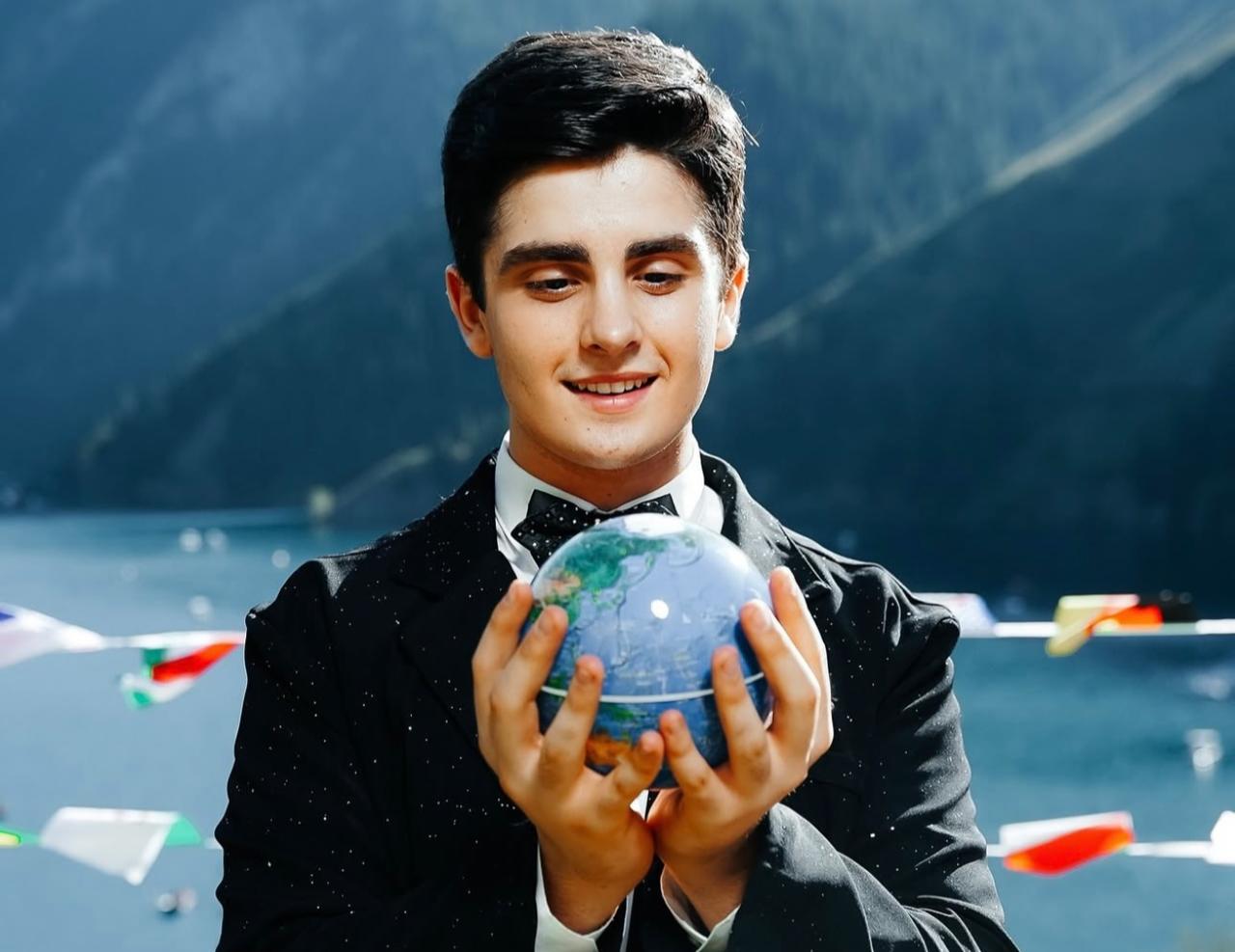 Omar Aliyev gazing at a globe against a mountain and lake backdrop. (Photo via Omar Aliyev's archive)