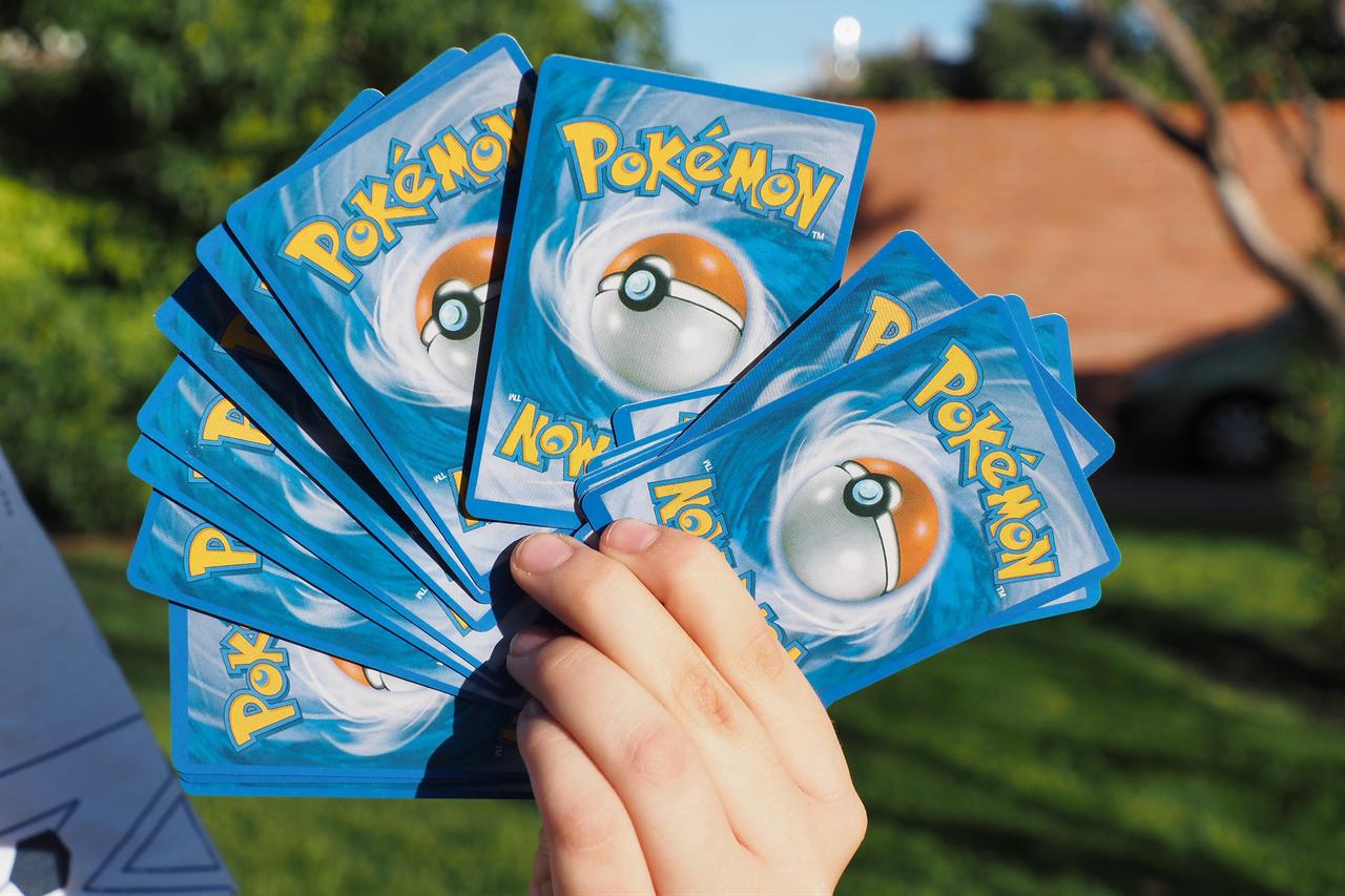 A person holds several Pokémon trading cards with the classic blue-backed design featuring a Poké Ball. (Adobe Stock Photo)