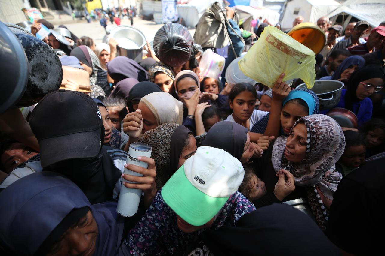 Palestinians, including children, wait with their containers to receive hot meals distributed by charity organizations, as people struggle with hunger due to the Israeli food blockade at Nuseirat refugee camp in Gaza City, Gaza, on Sept. 27, 2025. (AA Photo)