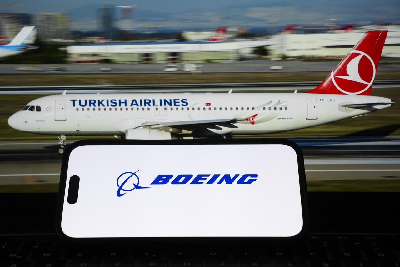 In this photo illustration, the Boeing and Turkish Airlines logos are displayed on a mobile phone through a magnifying glass in front of a Turkish Airlines plane shown on a screen in Ankara, Türkiye. (AA Photo)