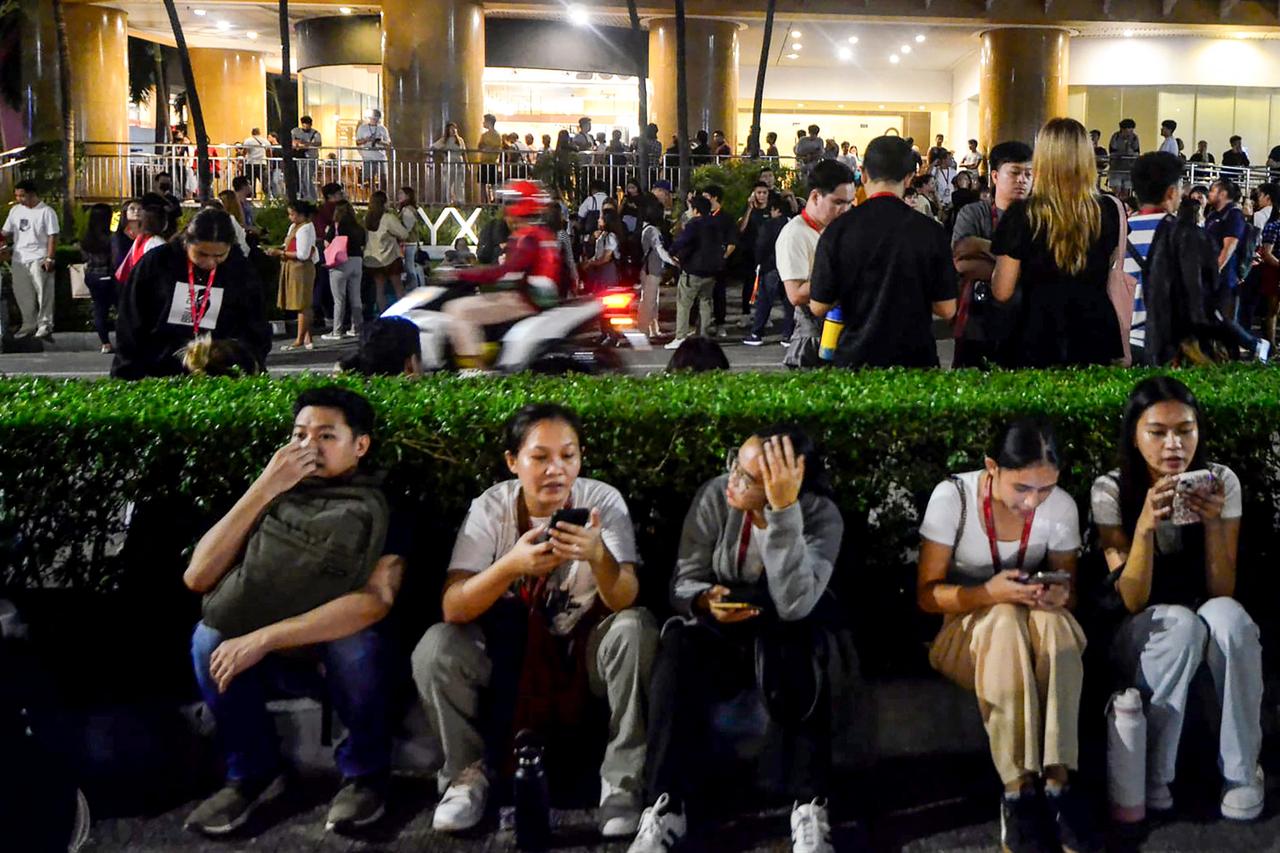 Call center employees surf mobile phones as they gather outside their office building after earthquake tremors at Cebu in central Philippines, Sept. 30, 2025. (AFP Photo)