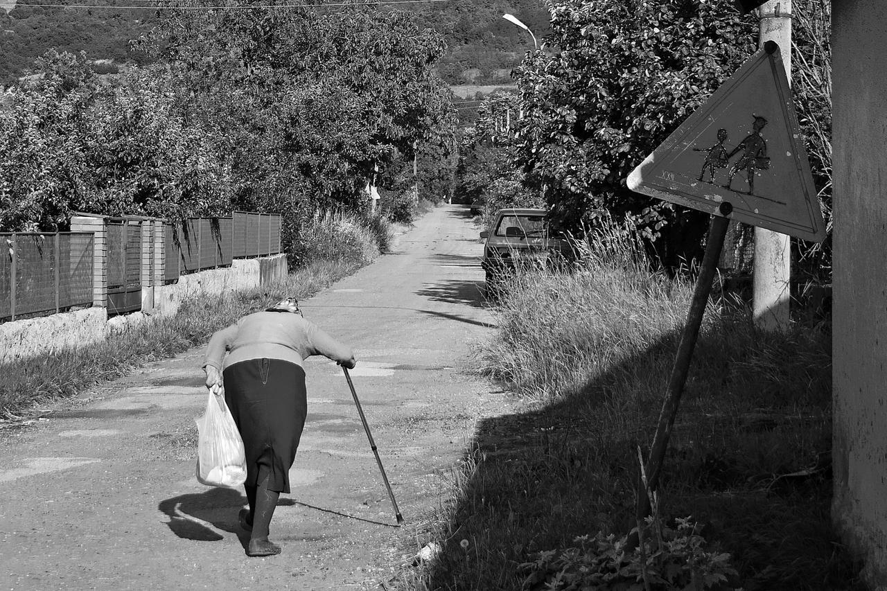 An elderly woman walks with a cane along a quiet country road. (Adobe Stock Photo)