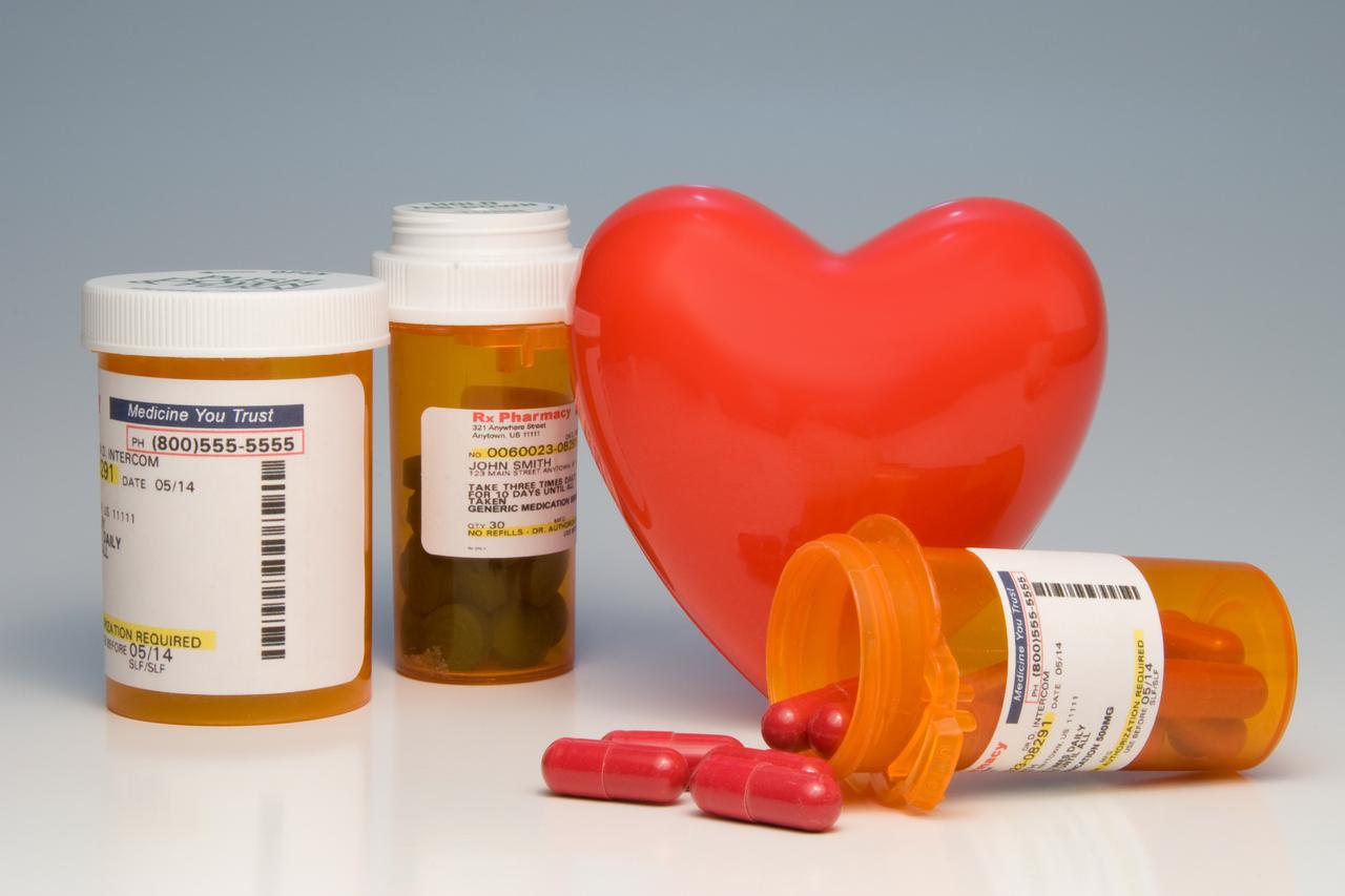 A symbolic heart surrounded by bottles of prescription medication. (Adobe Stock Photo)