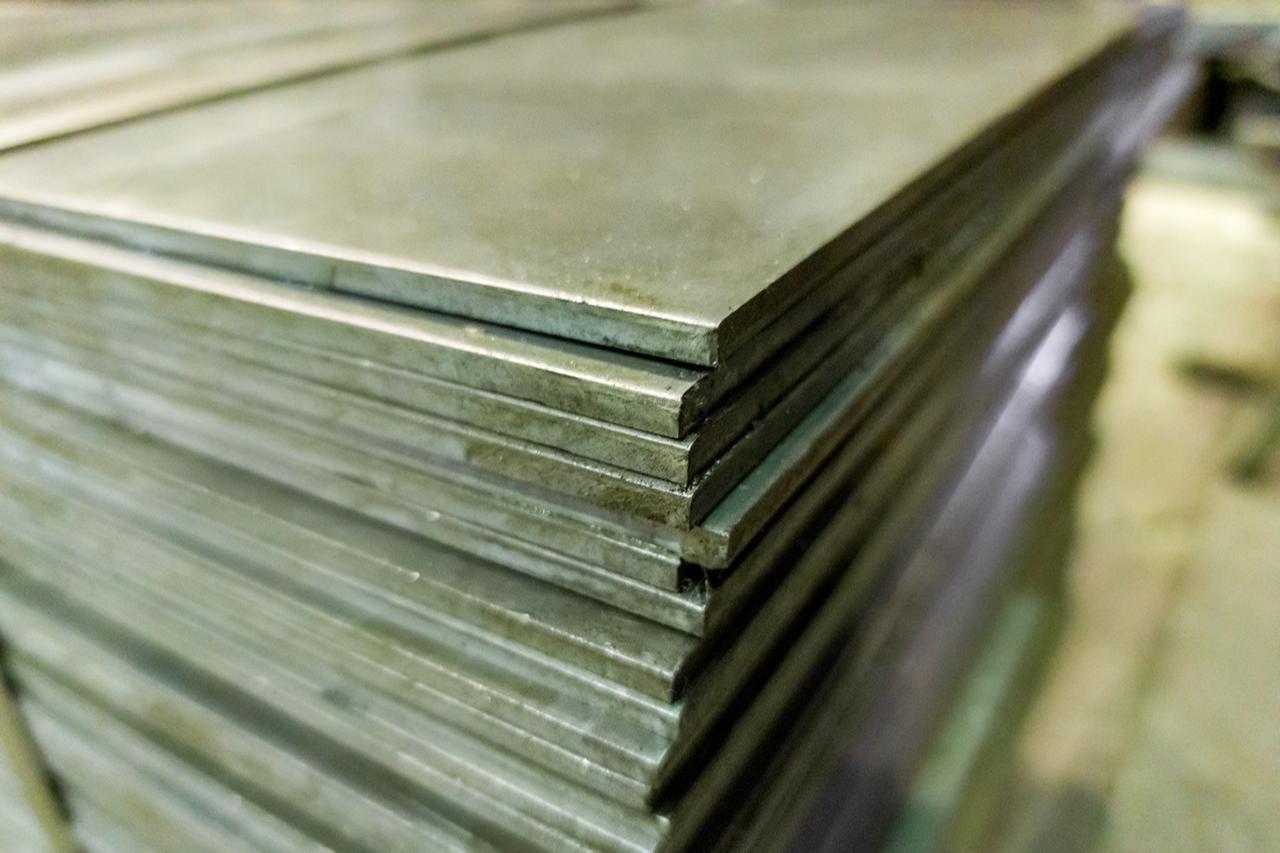 Stacks of thick-rolled steel sheets stored in a warehouse. (Adobe Stock Photo)