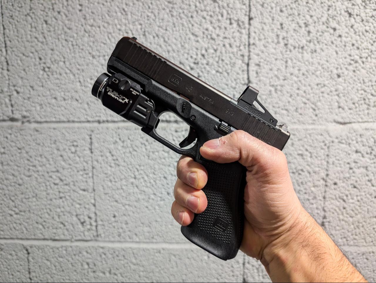 Glock 45 pistol with a red dot sight and flashlight in a person's hand against a wall, December 20, 2024. (Adobe Stock Photo)