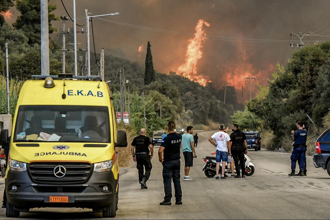 Police officers and inhabitants stand on a road as a wildfire burns a forest near the city of Patras, western Greece, August 12, 2025. (AFP Photo)