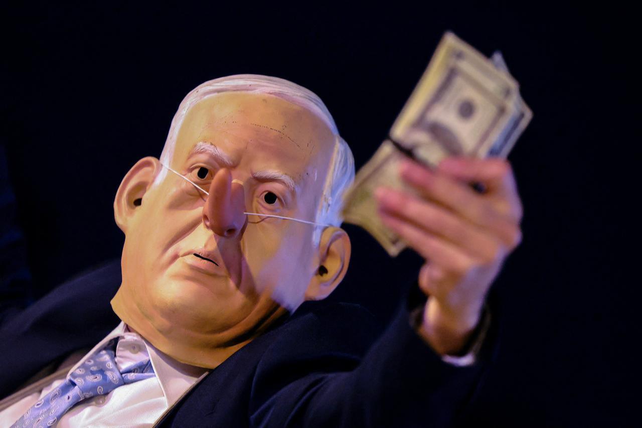 A protester wearing a mask depicting Israeli Prime Minister Benjamin Netanyahu holds a wad of cash during demonstration in Tel Aviv on January 3, 2026. (AFP Photo)